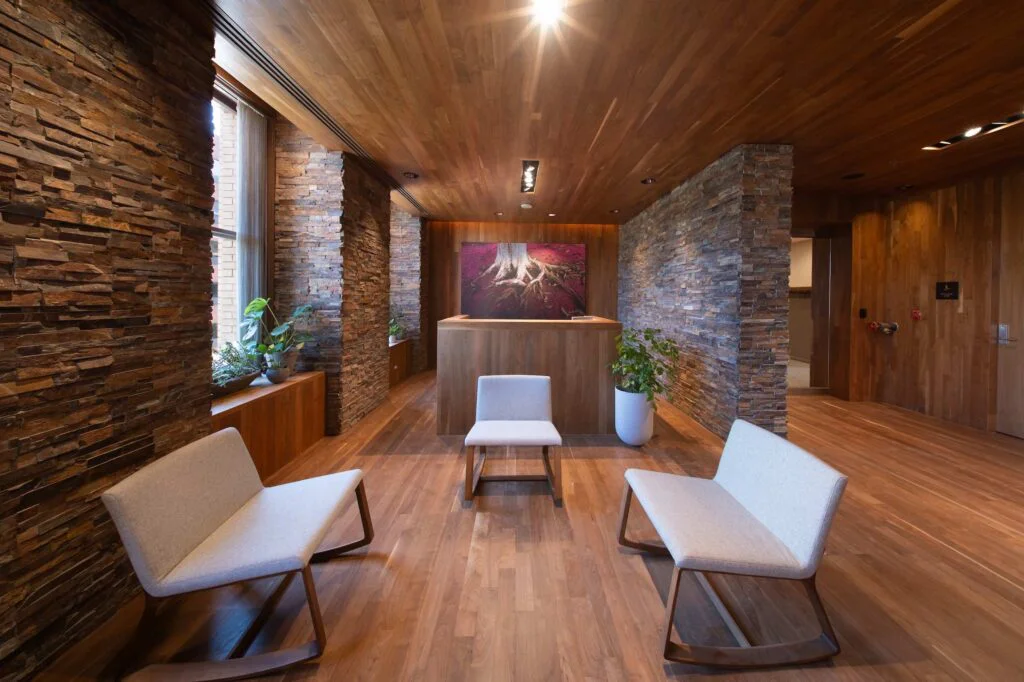 Reception lobby with walnut flooring, stacked stone columns, and a large tree root photograph above the front desk