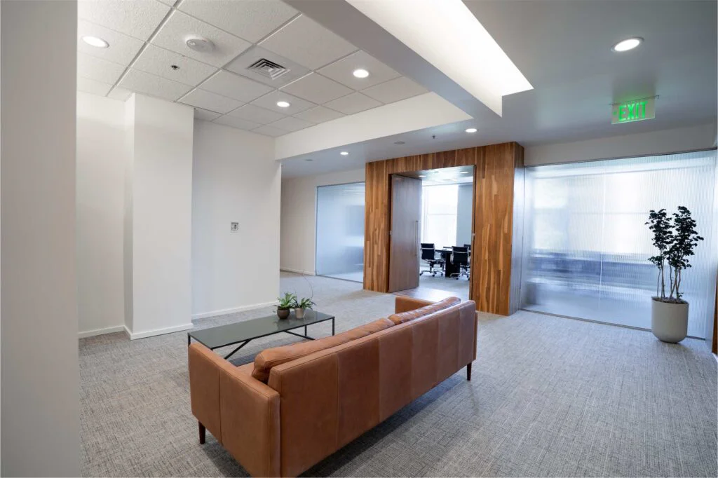 Leather sofa and glass coffee table in a lounge area beside a wood-framed glass conference room
