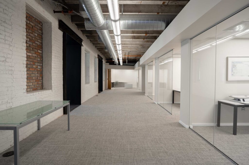 Long hallway with painted exposed brick, concrete ceiling, and glass-front offices along one side