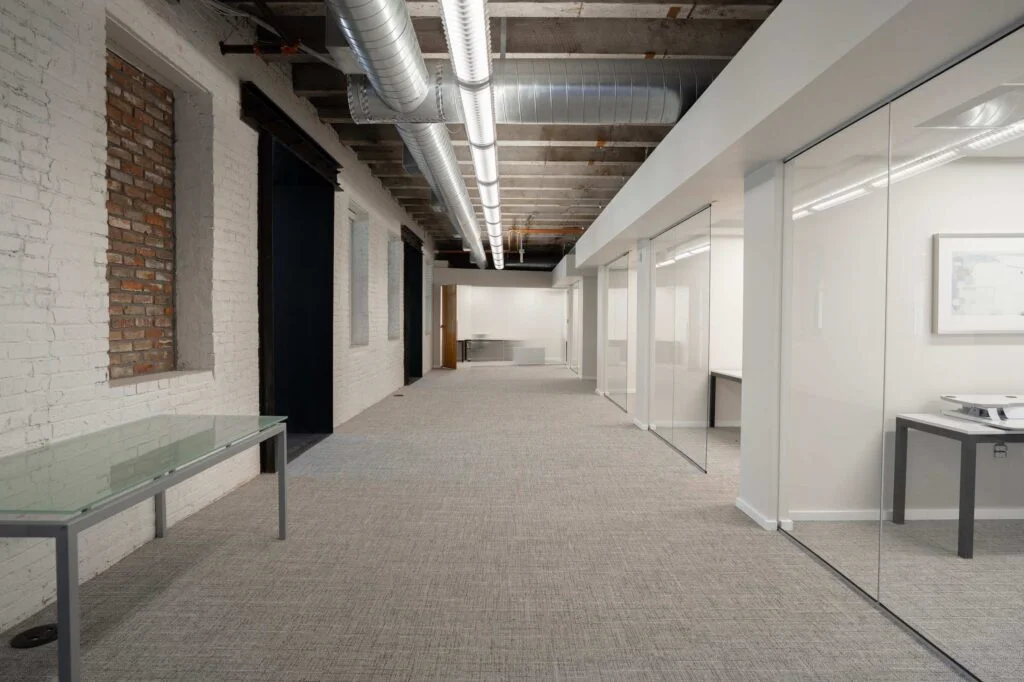 Long hallway with painted exposed brick, concrete ceiling, and glass-front offices along one side