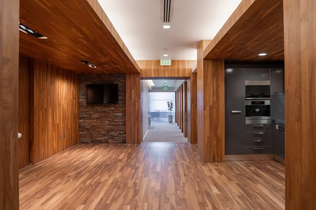 Walnut-paneled hallway with a mounted television on a stone accent wall and a built-in coffee station