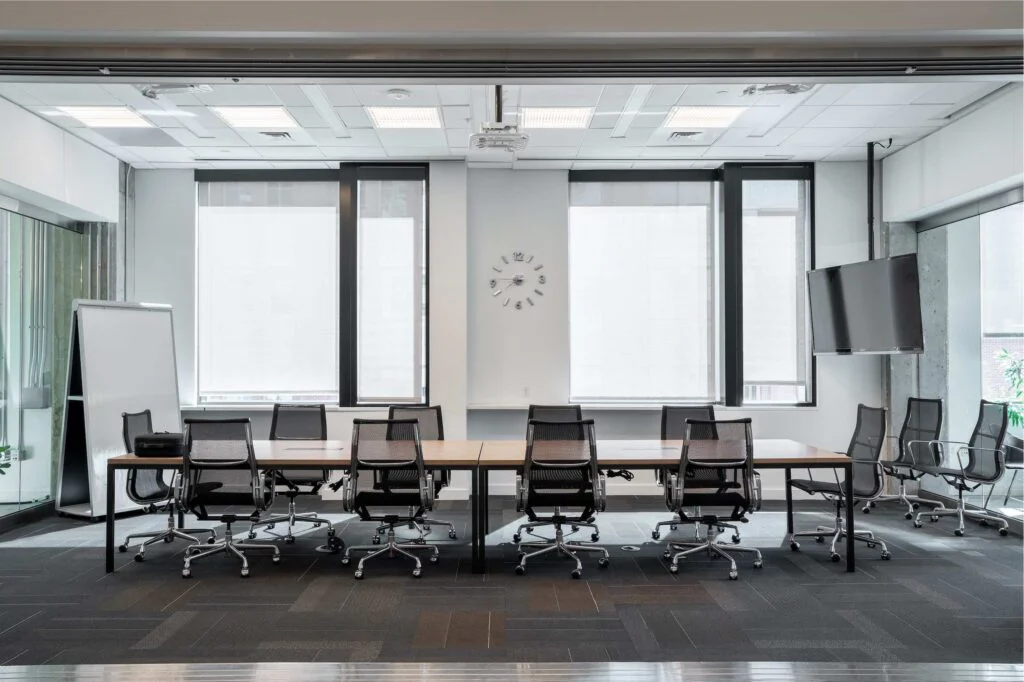 Long conference table with mesh chairs, wall-mounted TV, and curtained floor-to-ceiling windows