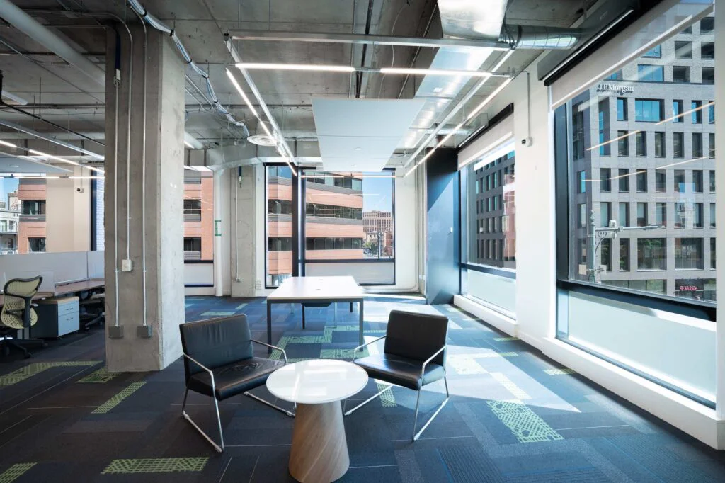 Small meeting table and two chairs beside floor-to-ceiling windows overlooking downtown office buildings