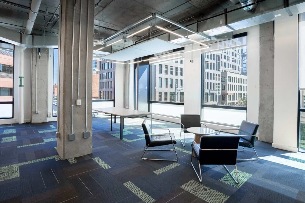 Leather chairs around a round wood table near a concrete column with panoramic downtown window views