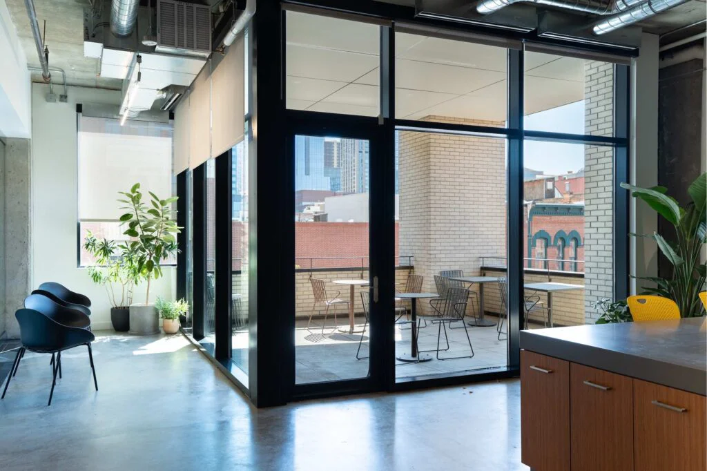 Glass sliding doors opening onto an outdoor terrace with cafe tables and chairs, brick buildings beyond