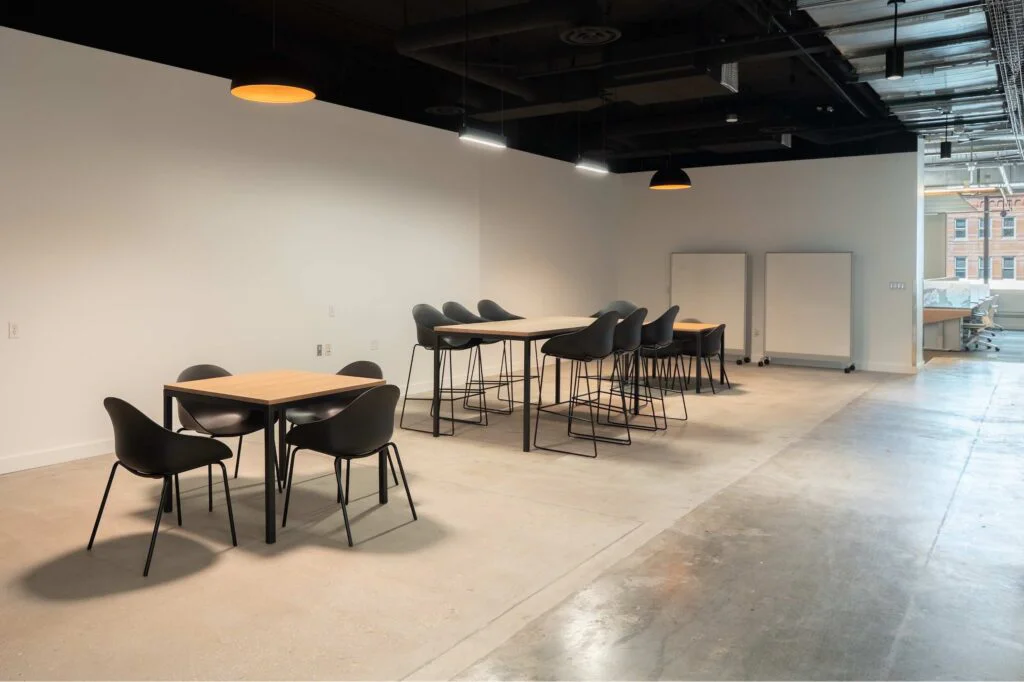 Casual seating with a bar-height table and mobile whiteboards, with a glass-walled conference room visible beyond