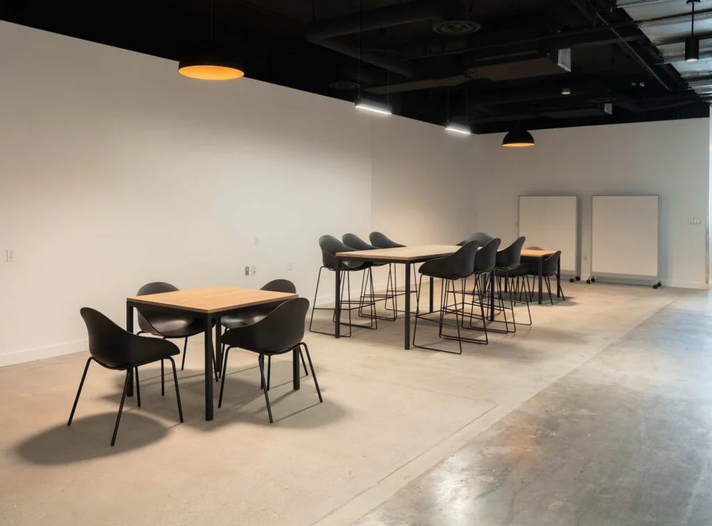 Small square table with chairs beside a standing-height bar table and mobile whiteboards in an open break area
