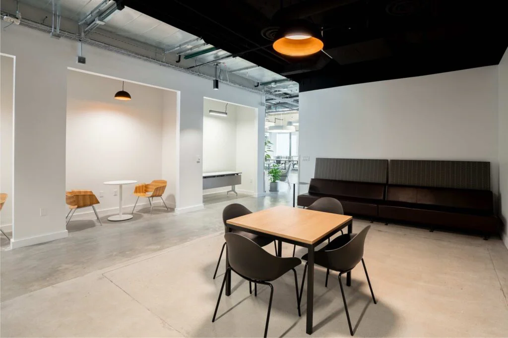 Wood lounge chairs in wall alcoves next to a long black booth bench and a wood meeting table