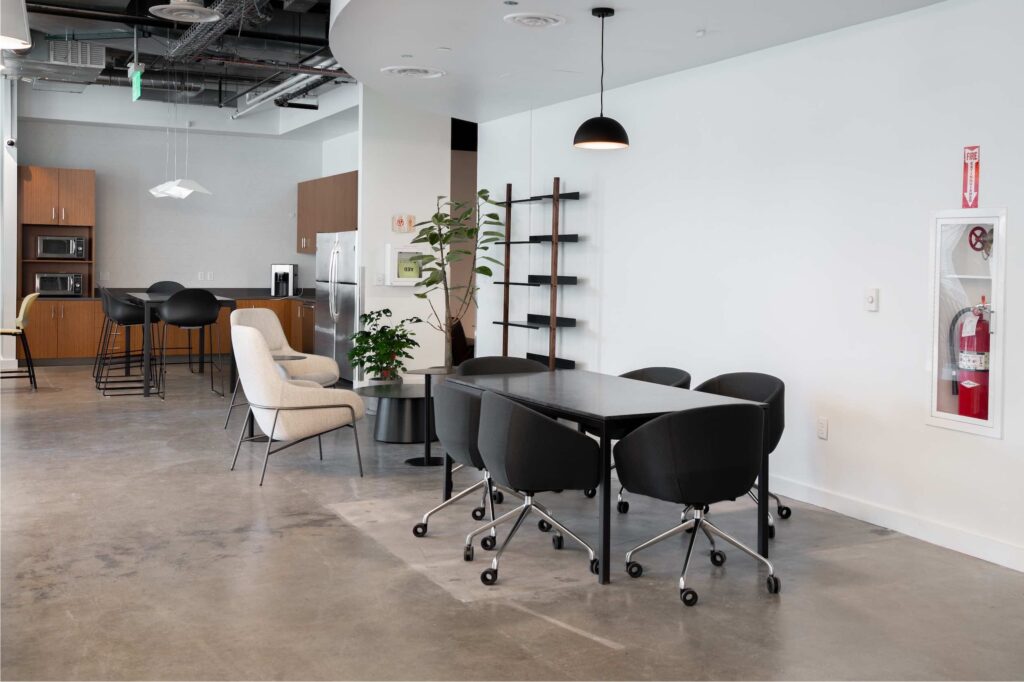Meeting table with rolling chairs near a kitchenette, wall ladder shelf, and cream lounge chair