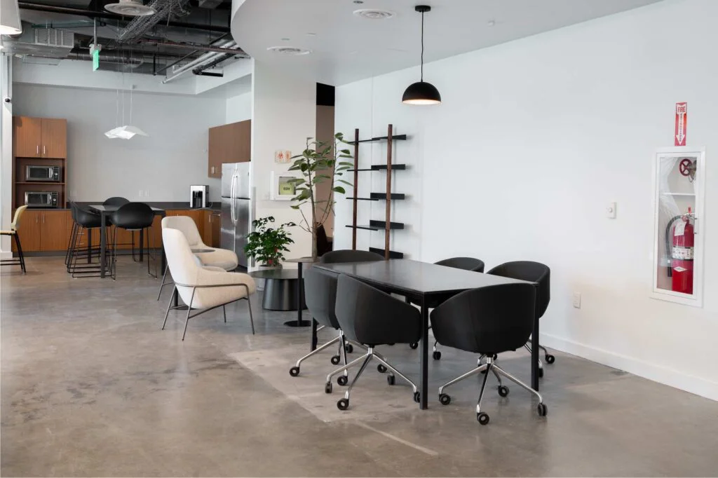 Meeting table with rolling chairs near a kitchenette, wall ladder shelf, and cream lounge chair