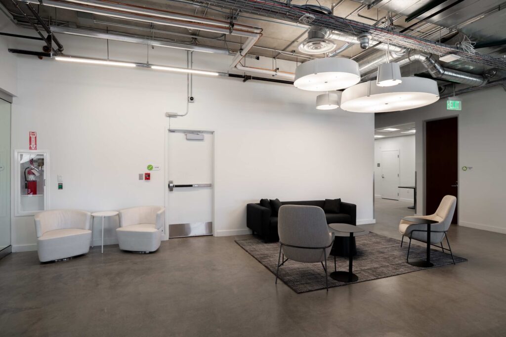 Seating area with white swivel chairs and a black sofa near a stairwell exit door