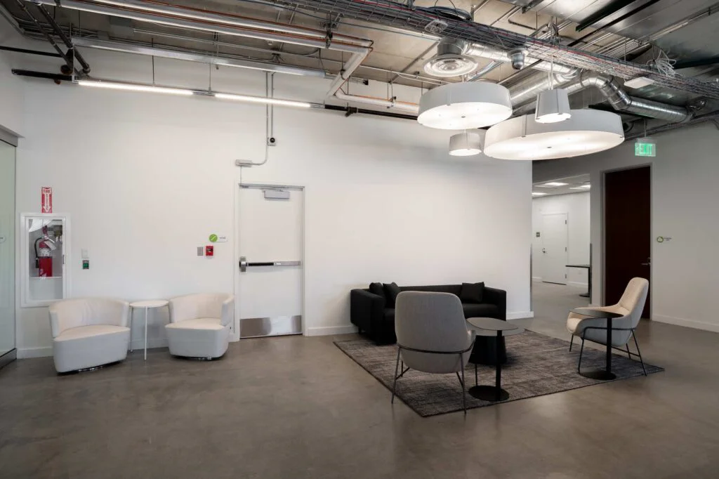 Seating area with white swivel chairs and a black sofa near a stairwell exit door
