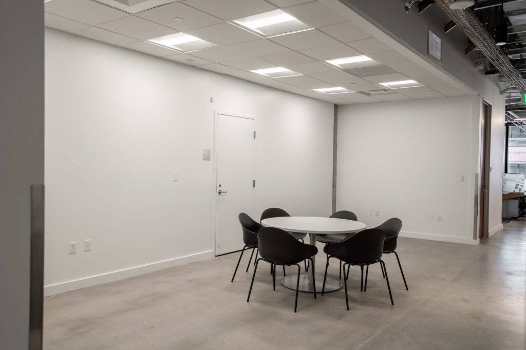 Small round meeting table with black chairs near an office entry door