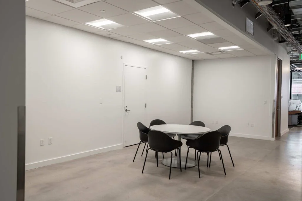 Small round meeting table with black chairs near an office entry door