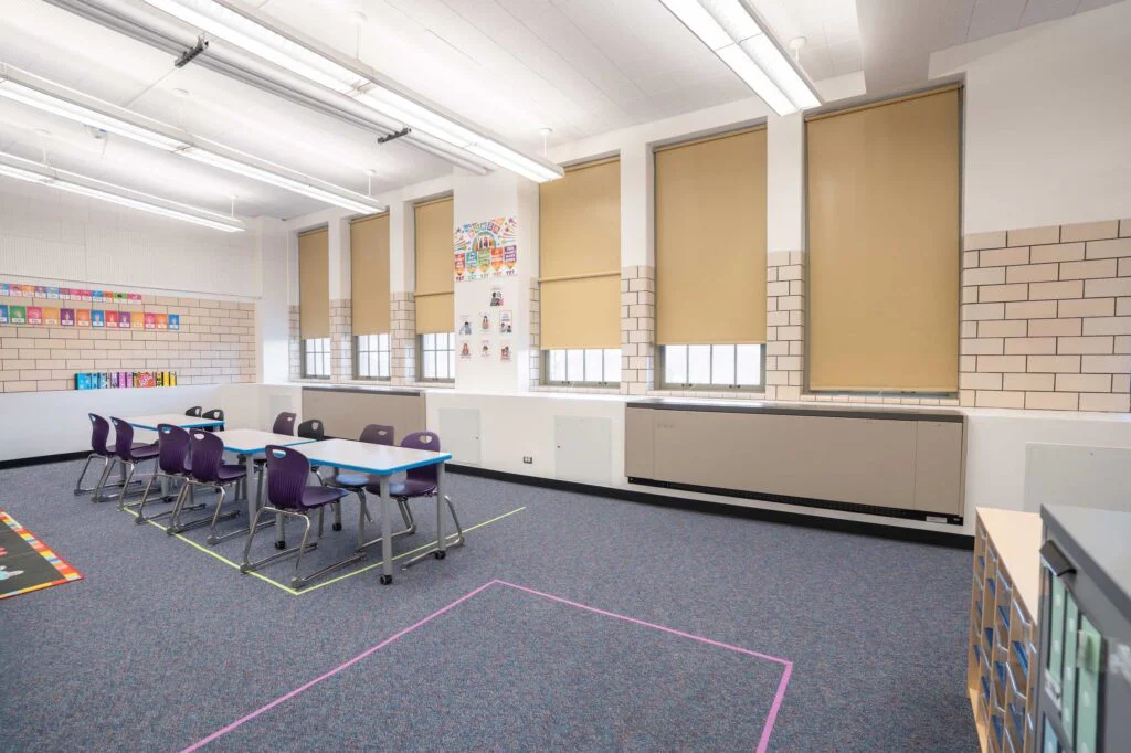 Elementary classroom with grouped student desks, purple chairs, and large windows
