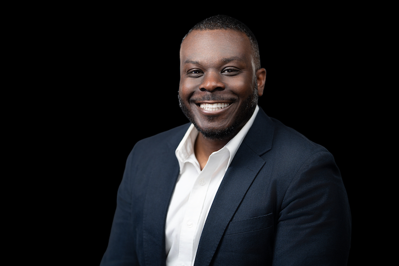 Professional headshot portrait of a man in a navy suit against a black background