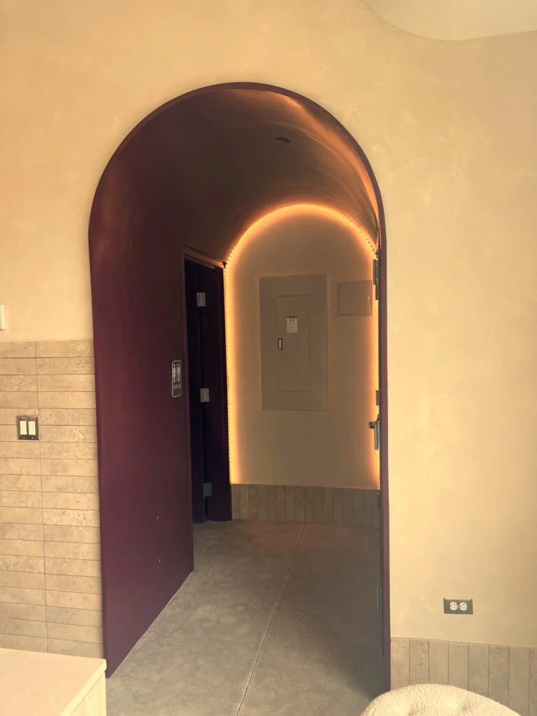 Open maroon archway doorway leading to a hallway with an electrical panel and restroom door