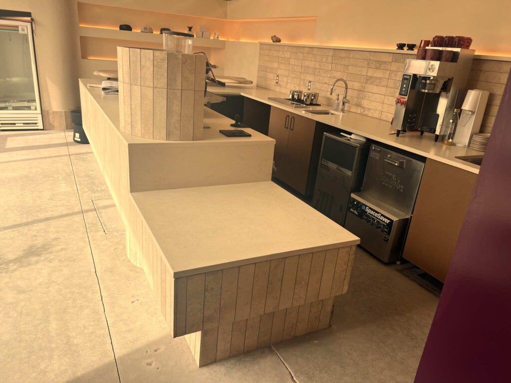 Tiled coffee counter with built-in sink, ice machine, and storage beneath a backlit display shelf