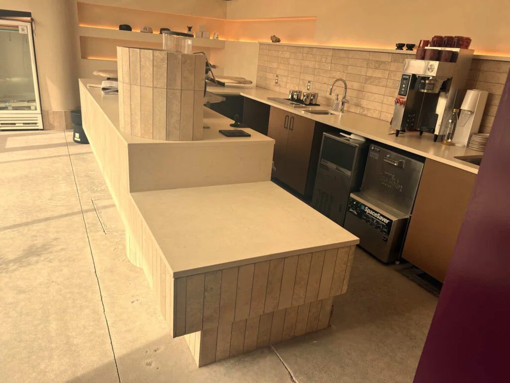 Tiled coffee counter with built-in sink, ice machine, and storage beneath a backlit display shelf