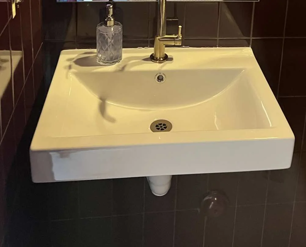 White ceramic sink with a brass gooseneck faucet against dark tile in a restroom