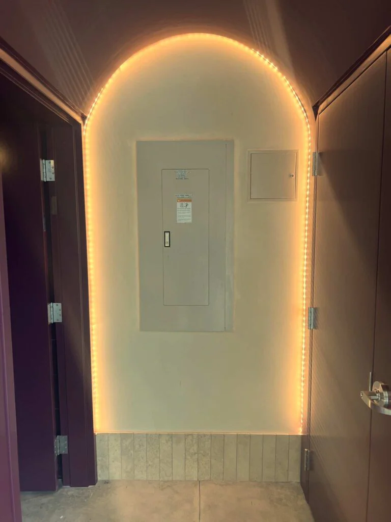 Arched doorway outlined in warm LED strip lighting leading to an electrical panel closet