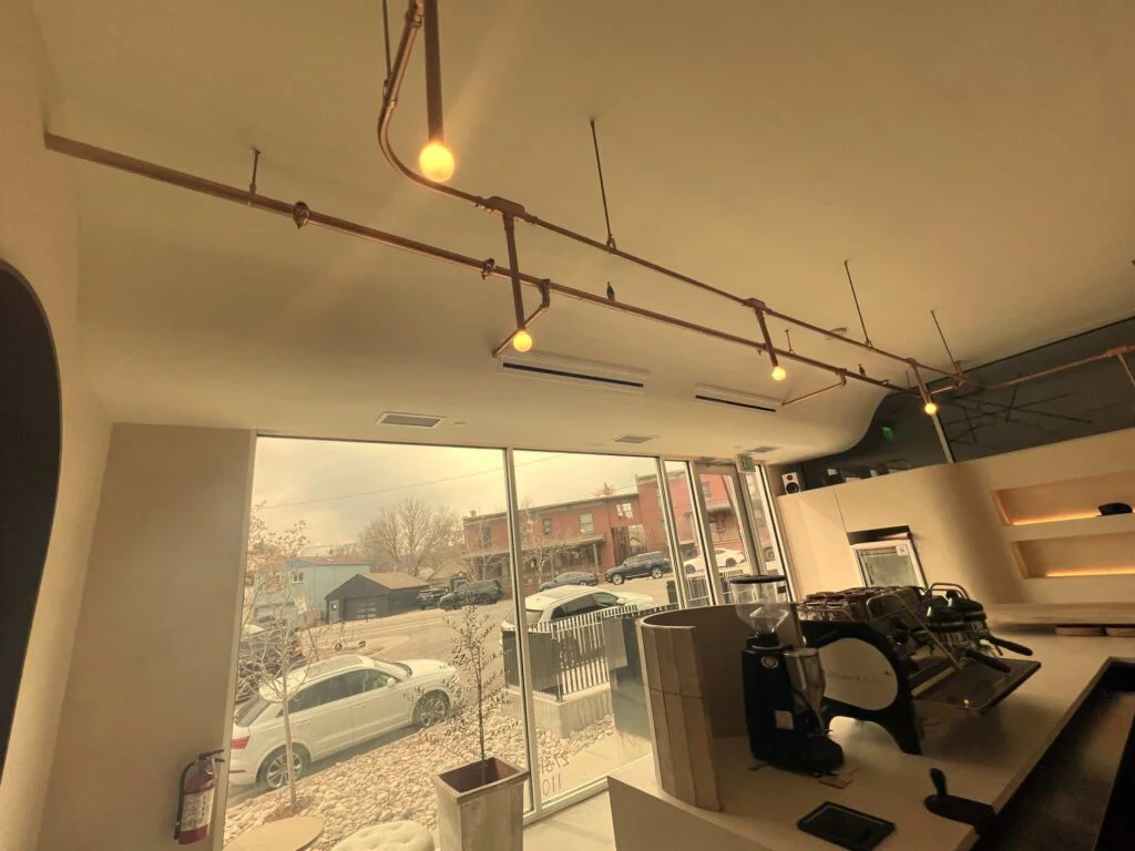 Upward view of copper pipe track lighting and ceiling vents above coffee shop storefront windows