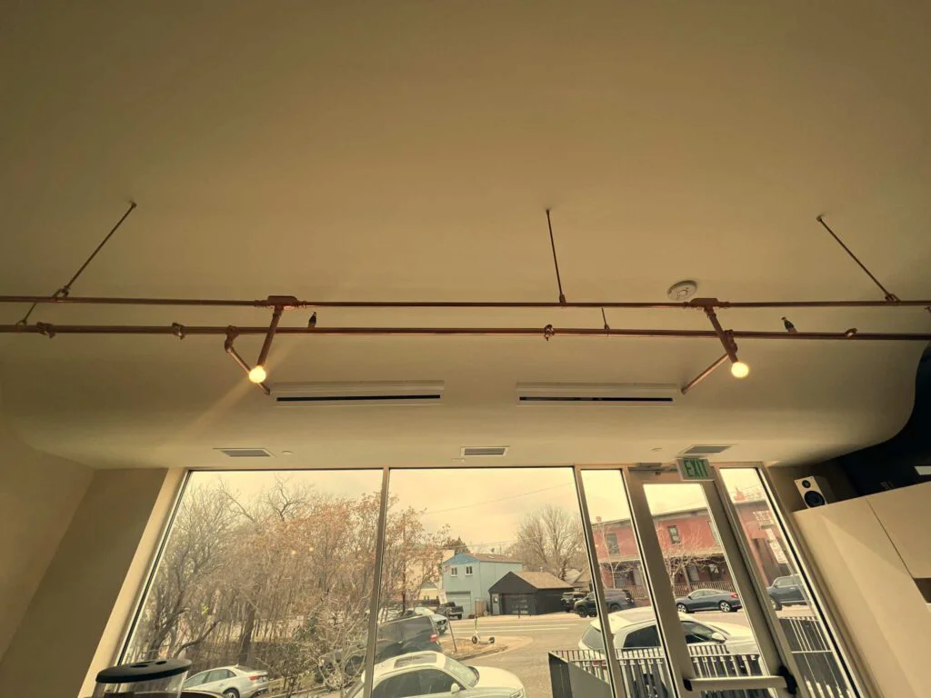 Close-up of exposed copper pipe track lighting with pendant bulbs along the ceiling