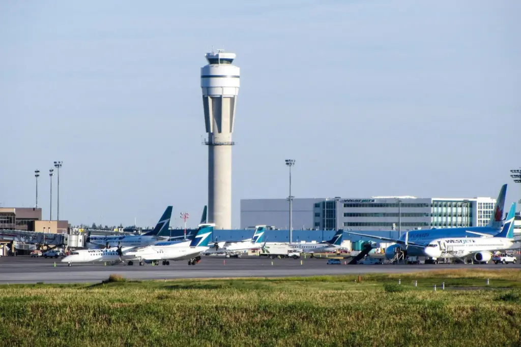 Airport tarmac with WestJet and Air Canada planes parked near the air traffic control tower